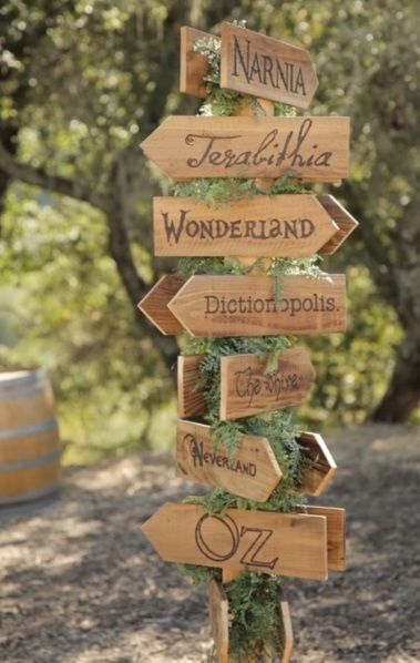 a wooden sign with many different signs on it in front of trees and dirt ground