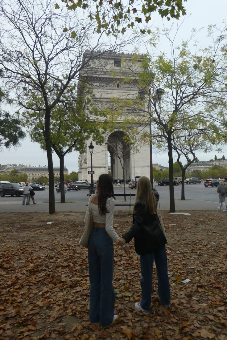 two women are standing in front of the arc de trioe, one holding her hand