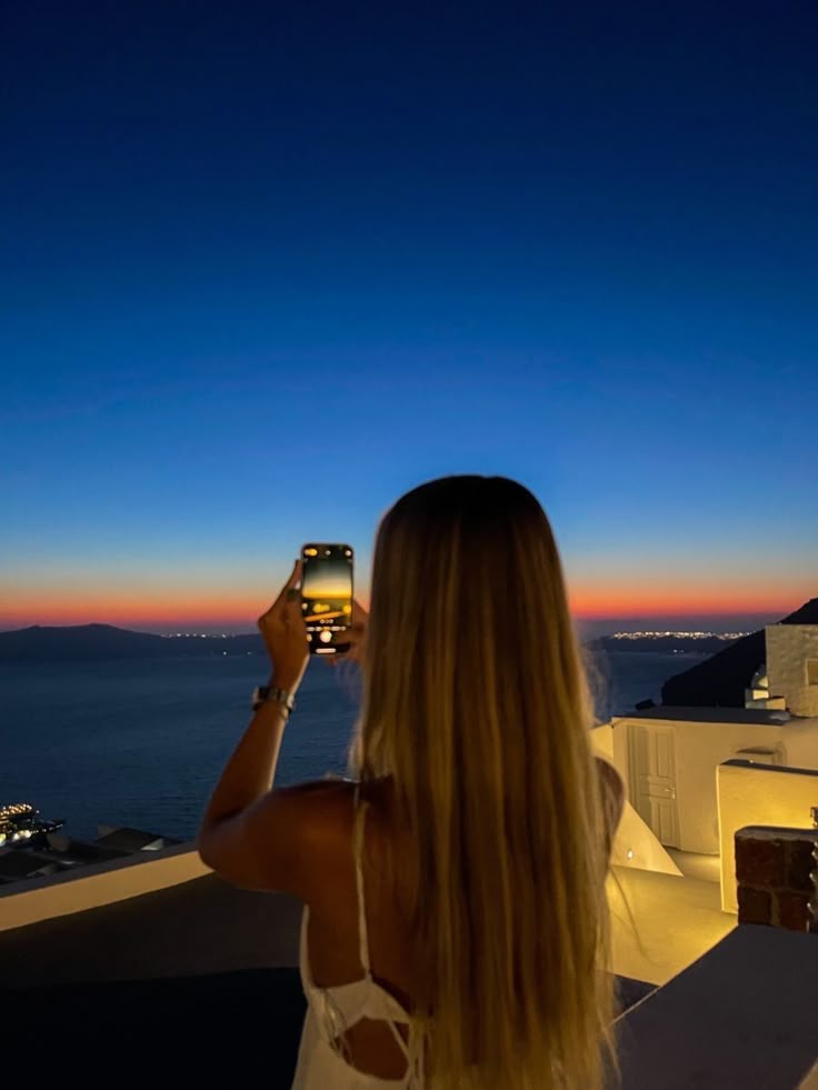 a woman standing on top of a roof looking at the sky with a cell phone in her hand