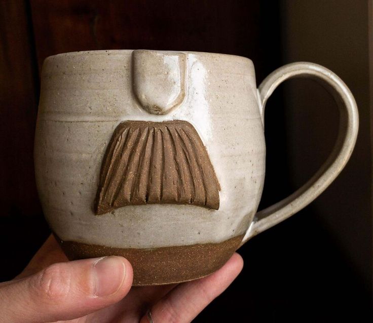 a hand holding a ceramic mug with a design on it's side and the handle