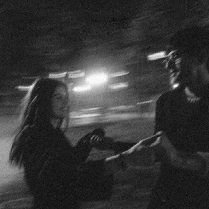 black and white photograph of two people standing next to each other in the street at night