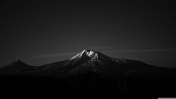 a black and white photo of the top of a mountain at night with clouds in the sky