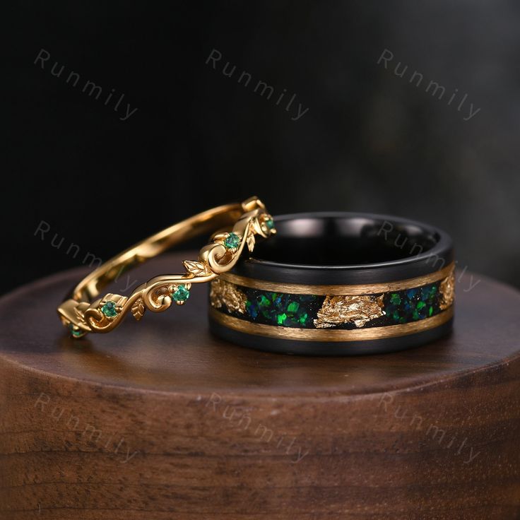 two wedding bands with green and gold designs on them sitting on a wooden stand in front of a black background