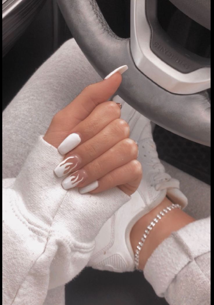 a woman's hand with white manicures on her nails, sitting next to a car steering wheel