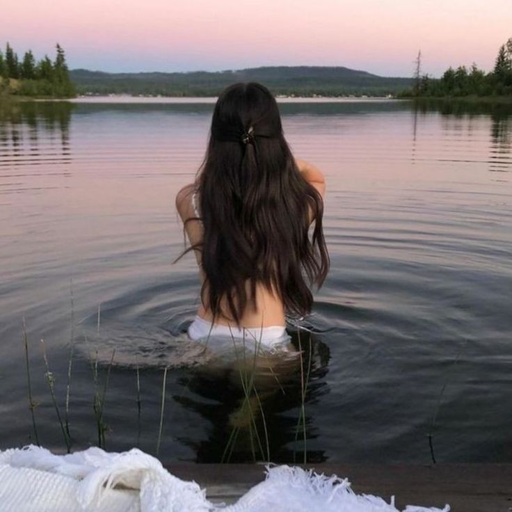 a woman is sitting in the water with her back to the camera and looking out at the lake