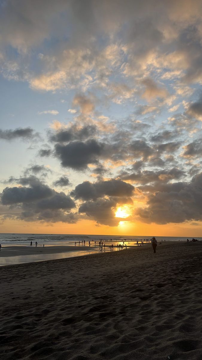 the sun is setting at the beach with people on it