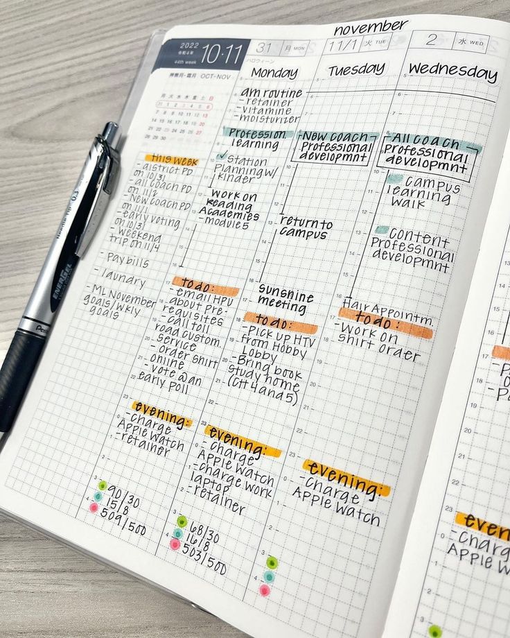 an open planner is shown on top of a wooden table with a pen in front of it