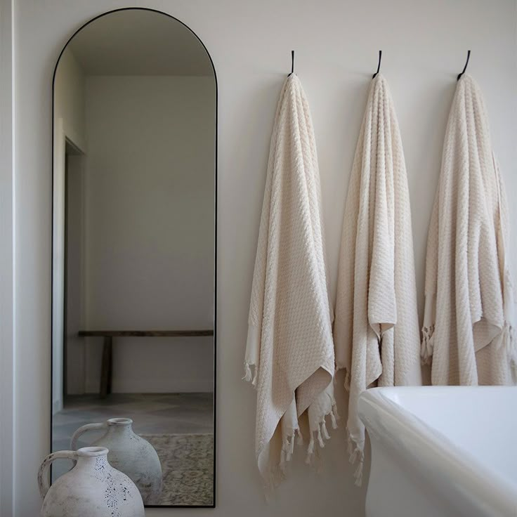 three towels hanging on the wall in front of a mirror and vase with an urn next to it