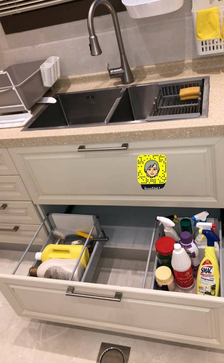 an open drawer in a kitchen filled with cleaning products and other household care items next to a sink