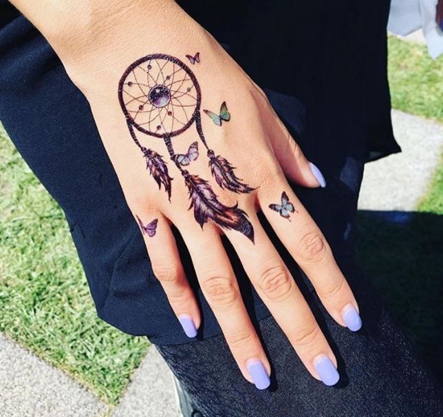 a woman's hand with a tattoo on it that has a dream catcher and butterflies