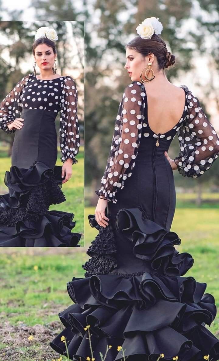 a woman wearing a black dress with polka dots on the top and bottom, standing in grass