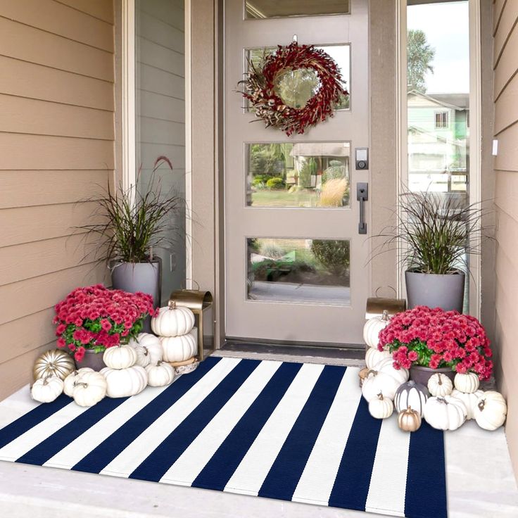 front porch decorated for fall with white pumpkins and red flowers on blue striped rug