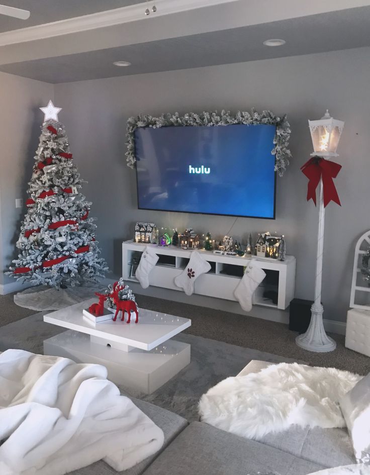 a living room decorated for christmas with white furniture and decorations on the walls, large flat screen tv