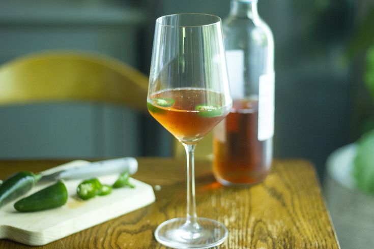 a wooden table topped with a wine glass filled with liquid next to a cutting board