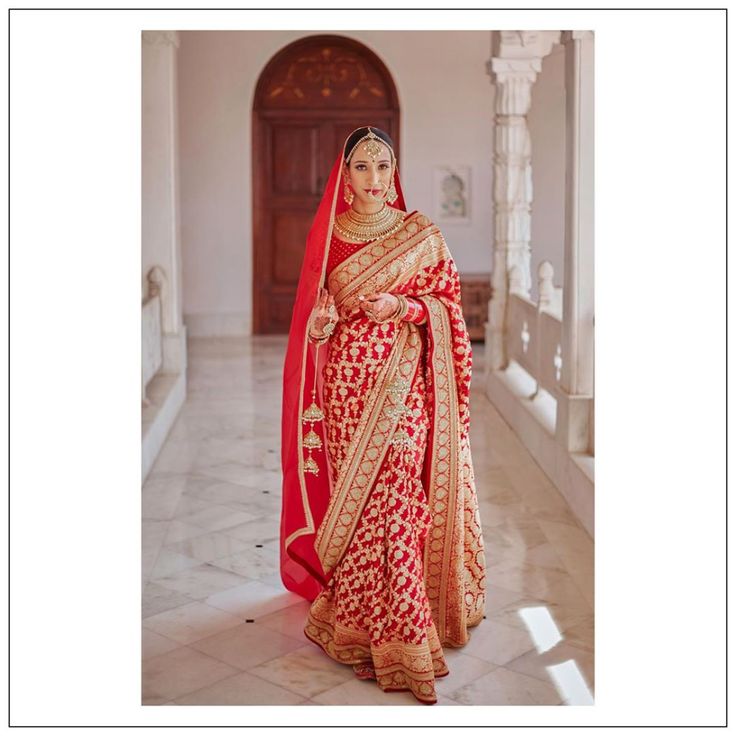 a woman in a red and gold bridal gown posing for the camera with her hands on her hips