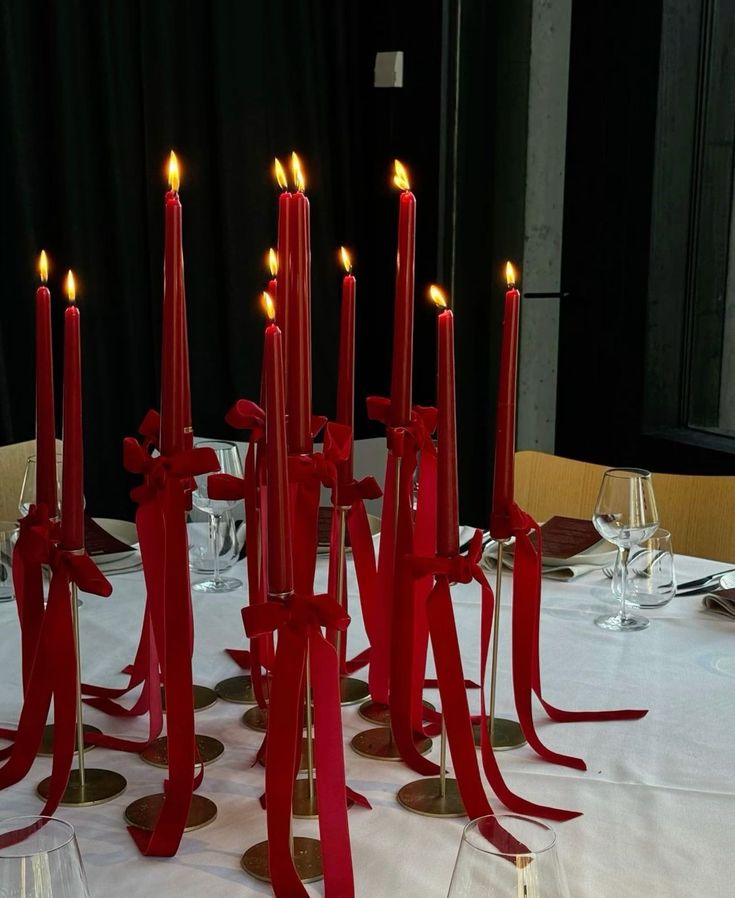 many red candles are on the table with wine glasses and silverware in front of them