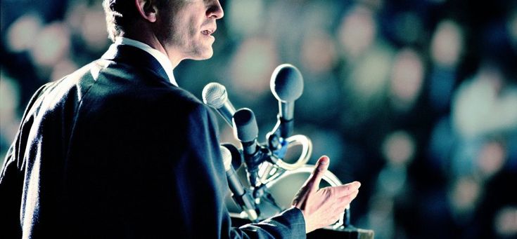 a man standing at a podium with microphones in front of him and looking off into the distance