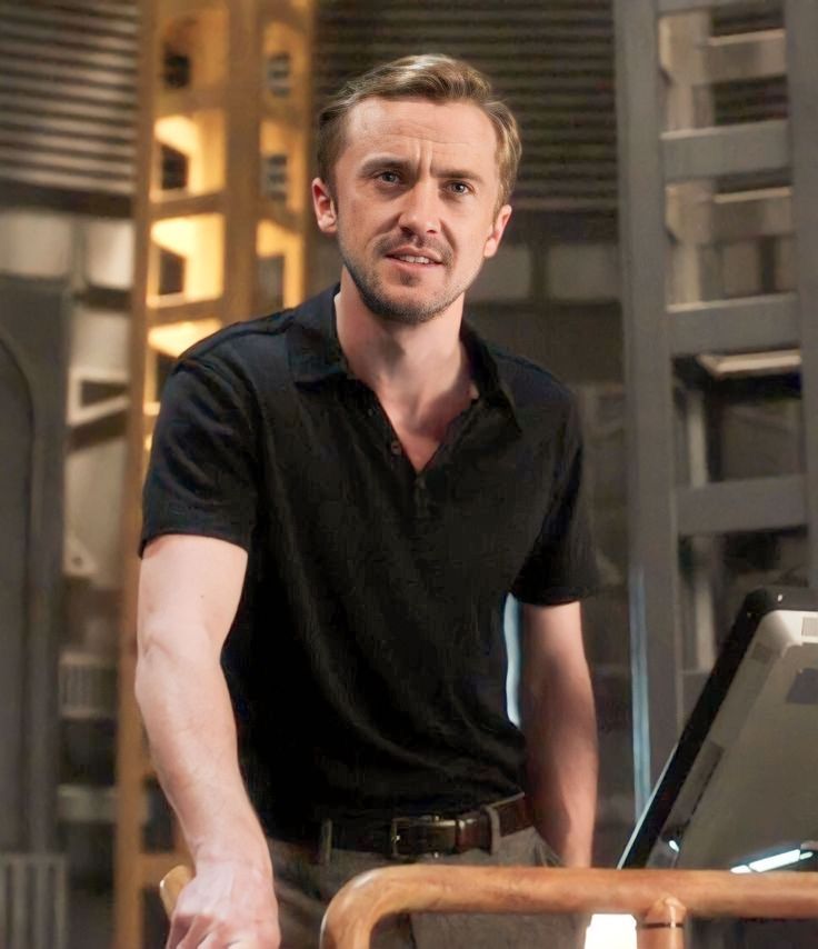 a man in black shirt standing next to a table with a laptop computer on it