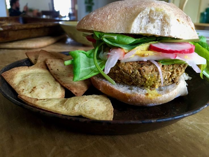 a sandwich with lettuce, tomato and onion on a plate next to chips