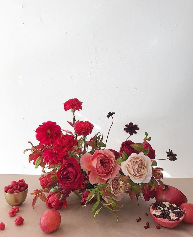 an arrangement of flowers and fruit on a table