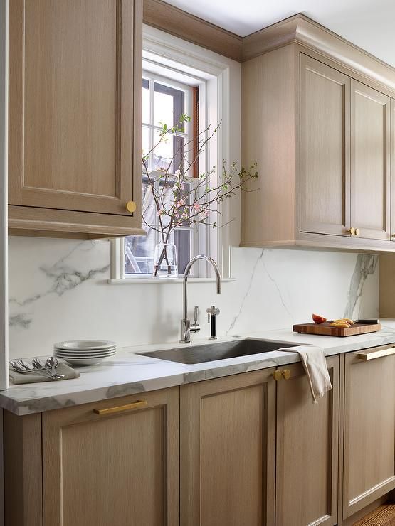 a kitchen with wooden cabinets and white marble counter tops, along with an open window