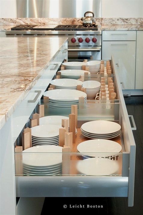 an open drawer in a kitchen filled with white plates and bowls next to a stove top oven