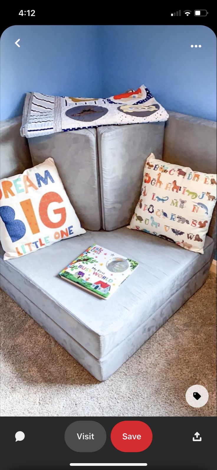 a gray couch with two pillows and a book on top of it in front of a blue wall