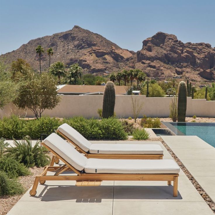 two chaise lounge chairs sitting in front of a pool with mountains in the background