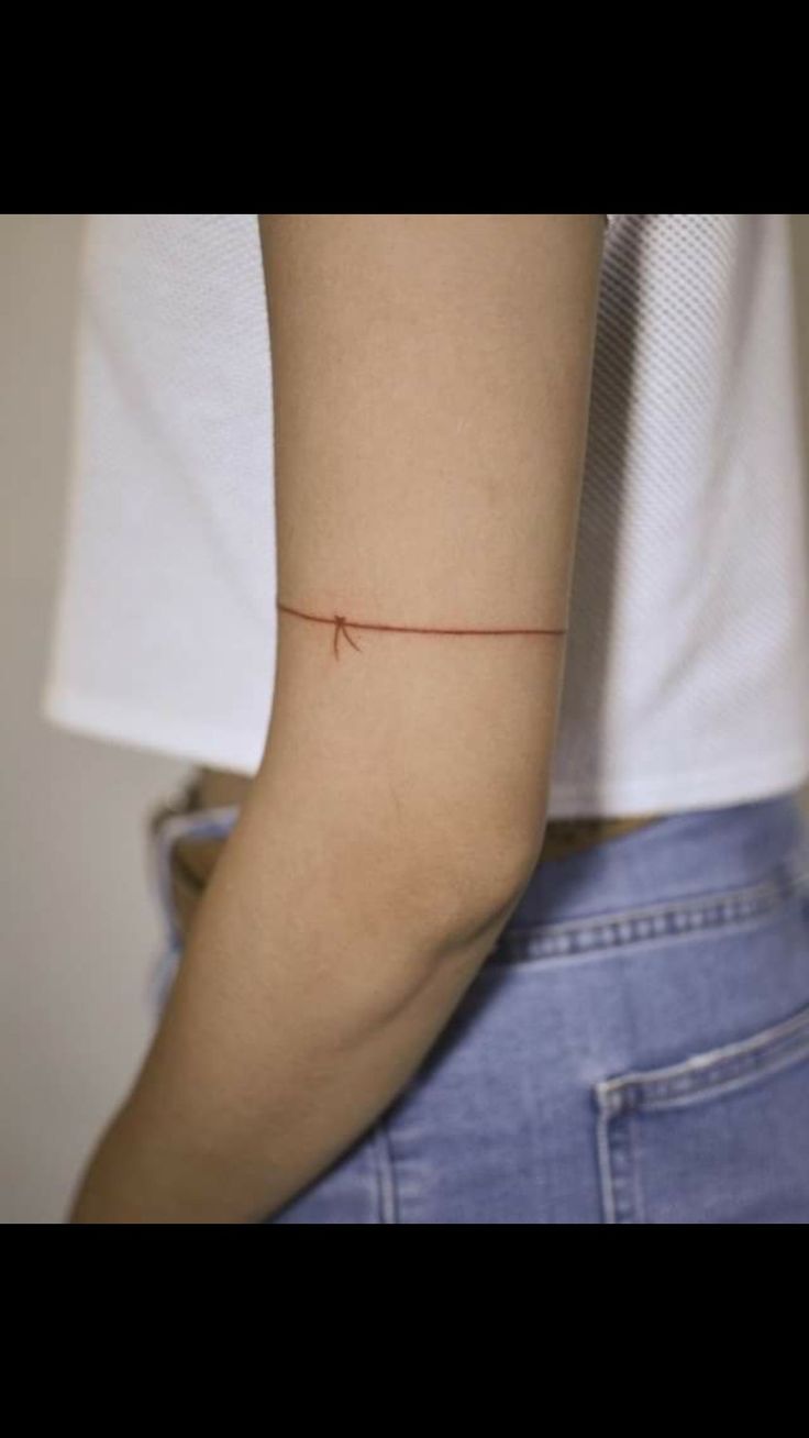 a woman's arm with a tiny red string tattoo on the left side of her arm