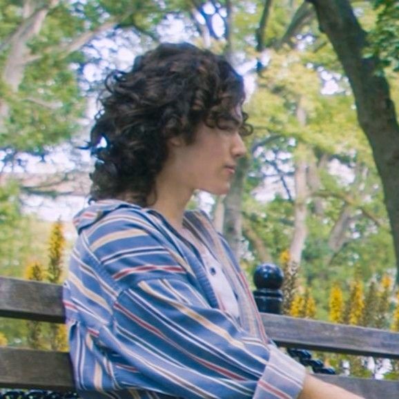 a woman sitting on top of a wooden bench in a park next to some trees