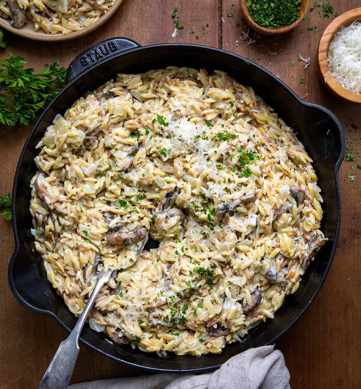 a skillet filled with pasta, mushrooms and parmesan cheese on a wooden table