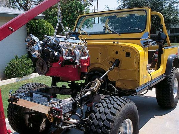 a yellow jeep is parked in front of a red truck with its hood up and engine on