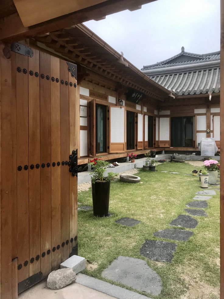 an open door leading to a courtyard with potted plants on the grass and stepping stones