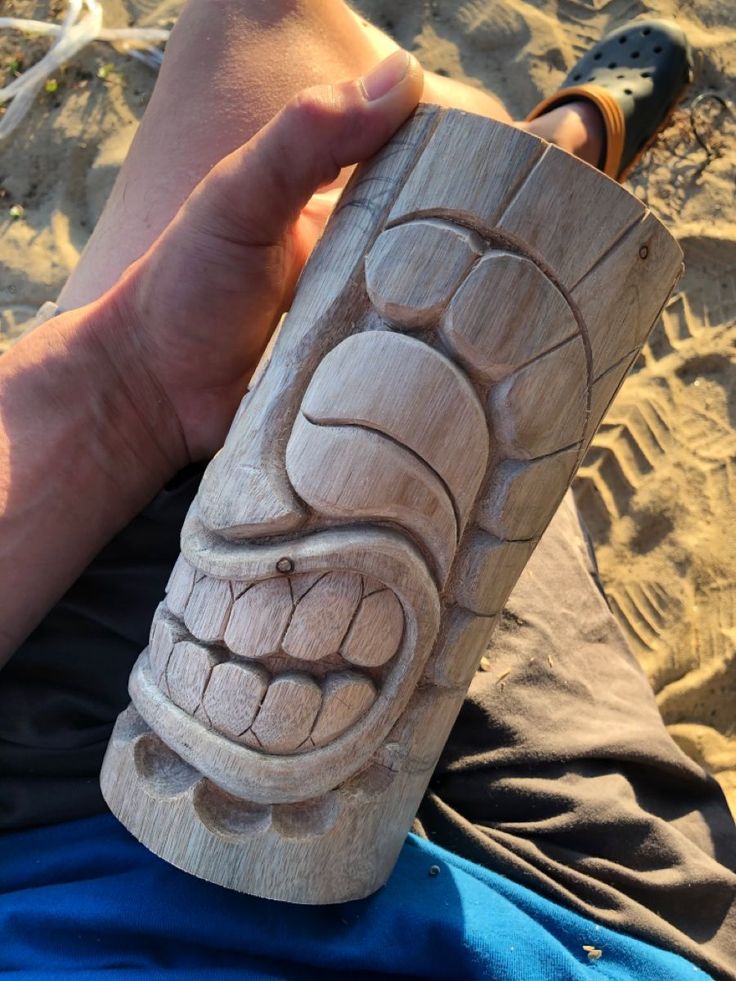 a person holding a carved wooden object in their hand on the beach with sand behind them