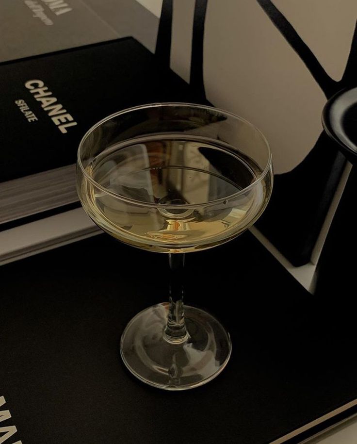 a glass of white wine sitting on top of a table next to a stack of books