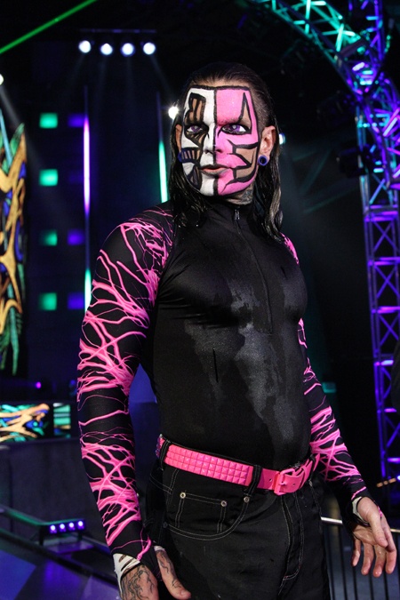 a man with his face painted in pink and black, standing on stage wearing a wrestling suit