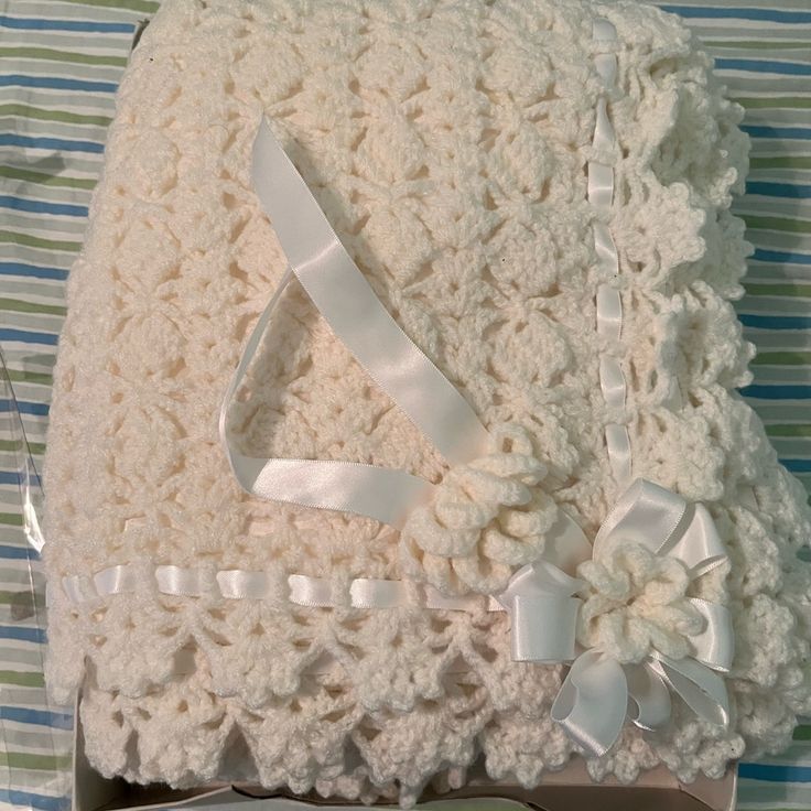 a crocheted blanket with white ribbon on it