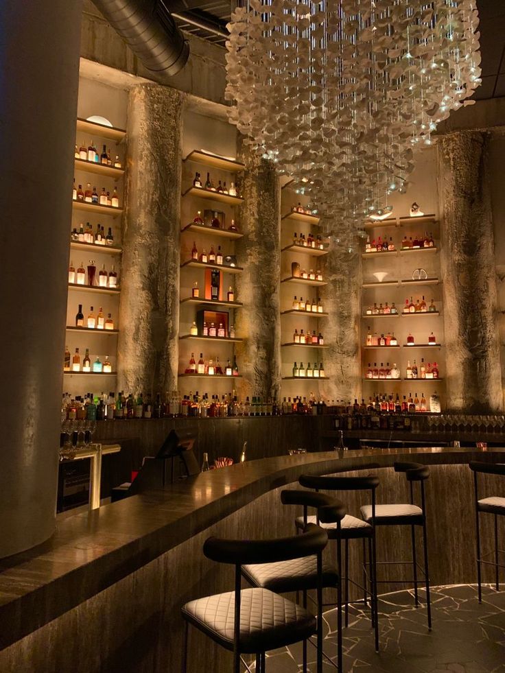 a dimly lit bar with lots of bottles on the shelves and chandelier hanging from the ceiling