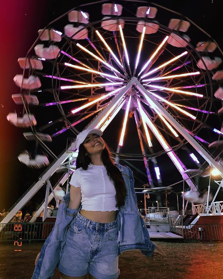 a woman standing in front of a ferris wheel at night with her hands on her hips