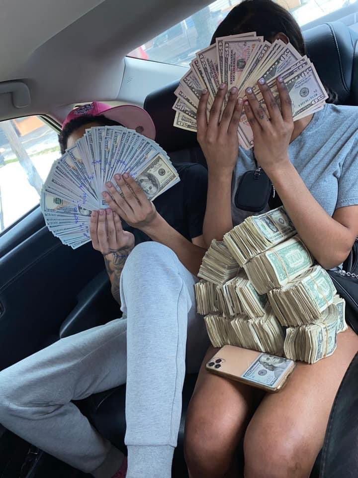 two people sitting in the back seat of a car with stacks of money covering their faces