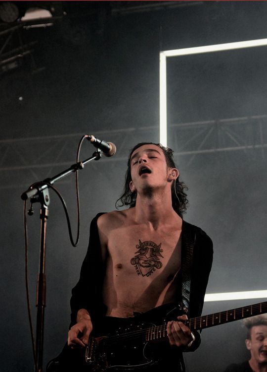 a man with no shirt on playing guitar in front of a microphone and two other men