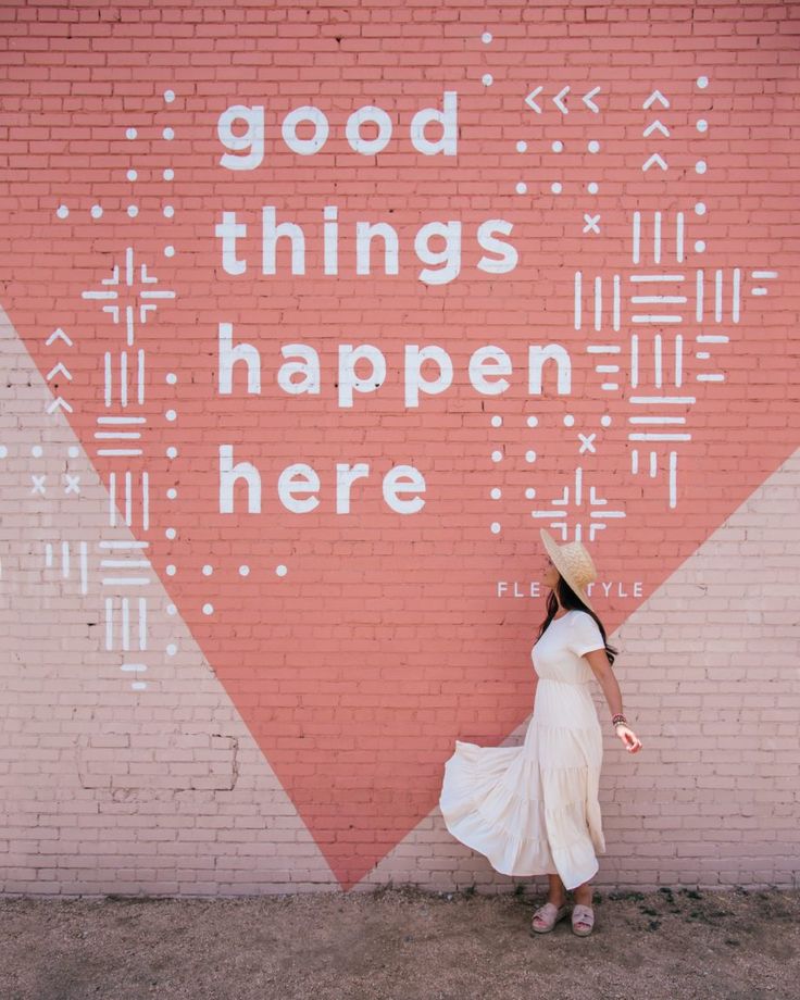 a woman standing in front of a brick wall with the words good things happen here painted on it