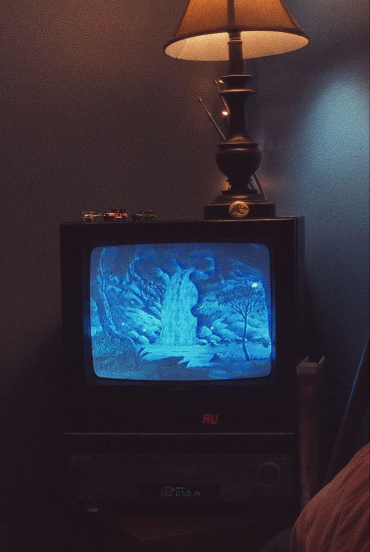 an old television sitting on top of a wooden table next to a lamp and a wall