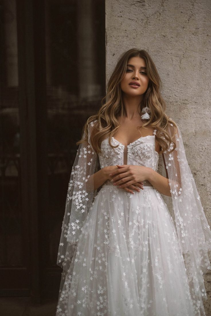 a woman in a white wedding dress standing next to a wall with her hands on her hips