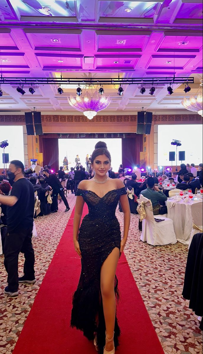 a woman in a long black dress is walking down the red carpeted hall at an event