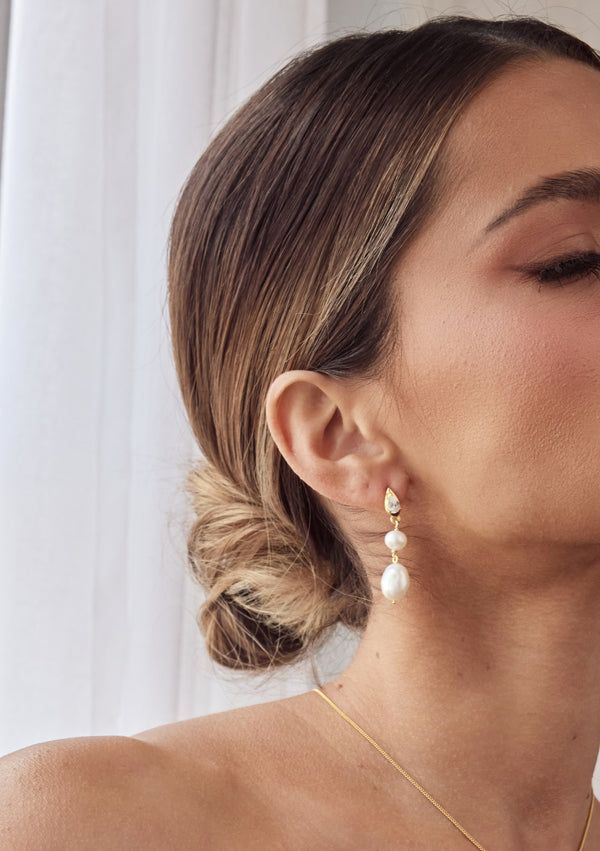 a woman wearing a gold necklace and earrings with white pearls on the bottom of her neck