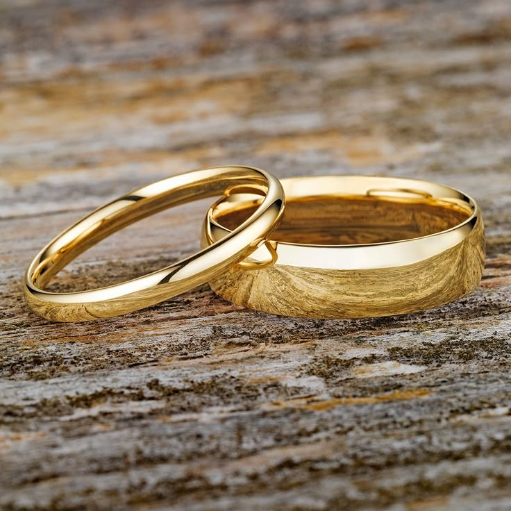 two gold wedding rings sitting on top of a piece of wood next to each other