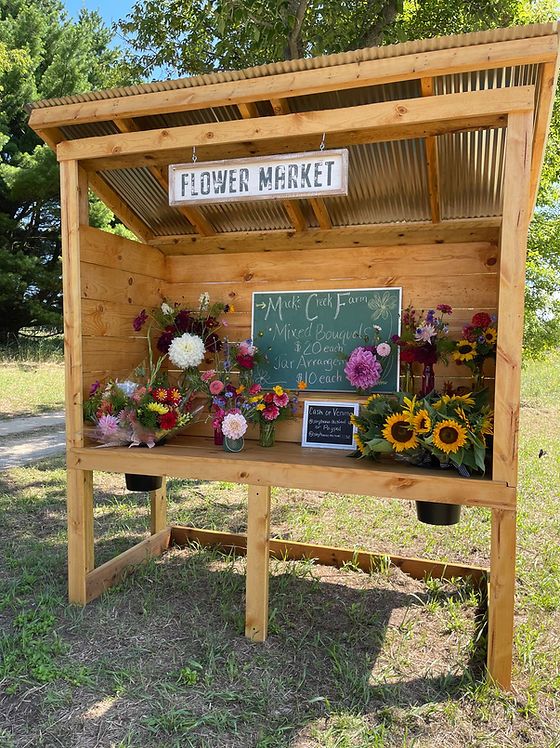 a flower market stand with flowers on the side and a chalkboard sign above it