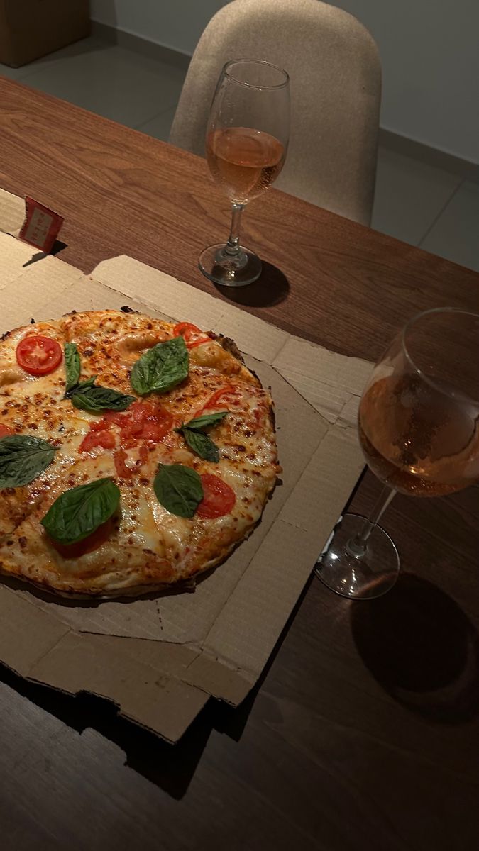 a pizza sitting on top of a cardboard box next to wine glasses and a book