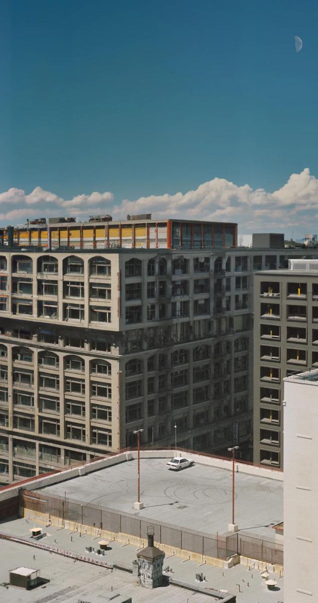 an aerial view of some buildings and parking lot in the foreground with clouds in the background